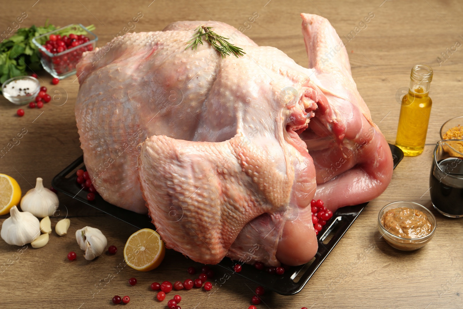 Photo of Whole raw turkey with ingredients for marinade on wooden table, closeup