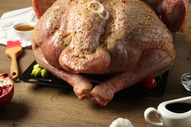 Photo of Whole raw turkey with ingredients for marinade on wooden table, closeup