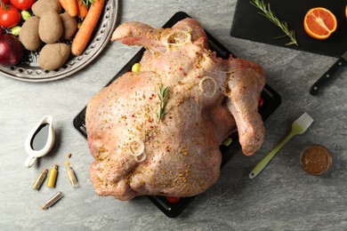 Photo of Whole raw turkey with ingredients for marinade and other products on grey table, flat lay