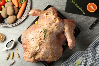 Photo of Whole raw turkey with ingredients for marinade and other products on grey table, flat lay