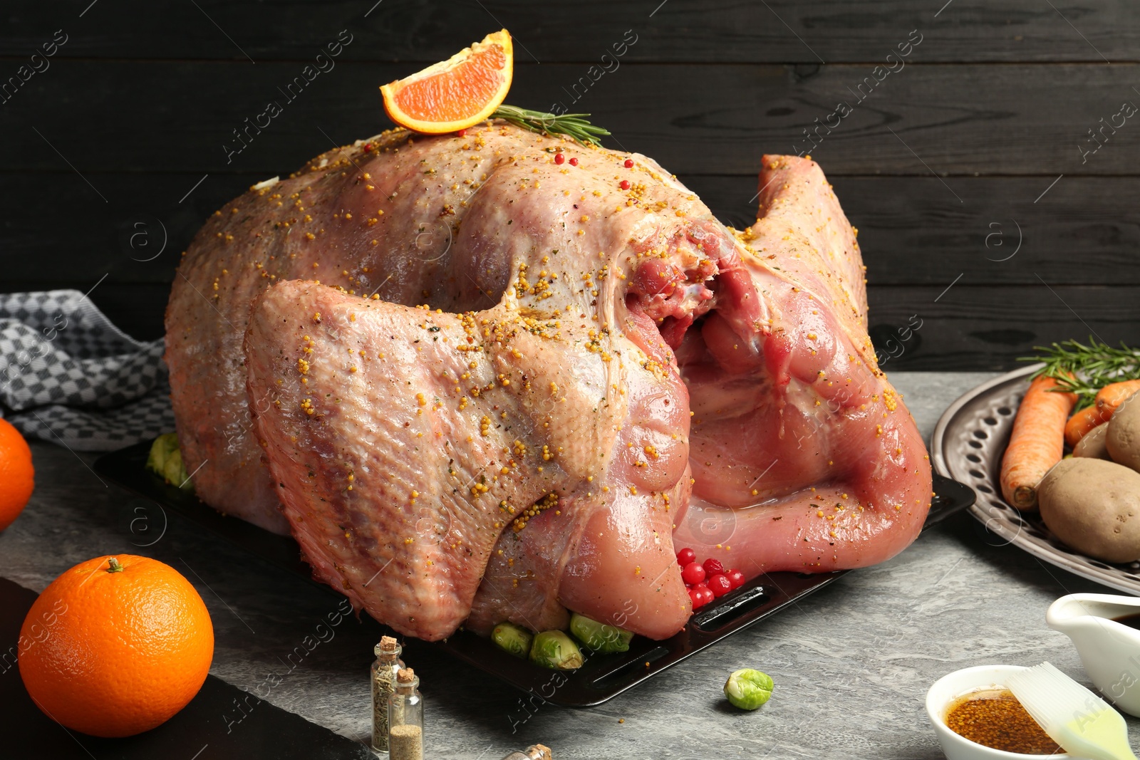 Photo of Whole raw turkey with ingredients for marinade and other products on grey table