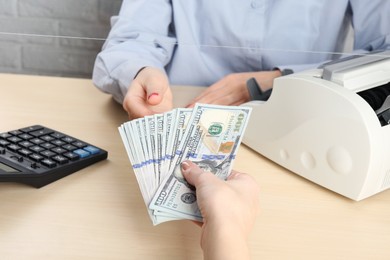 Photo of Client giving dollar banknotes to cashier at table in money exchange, closeup