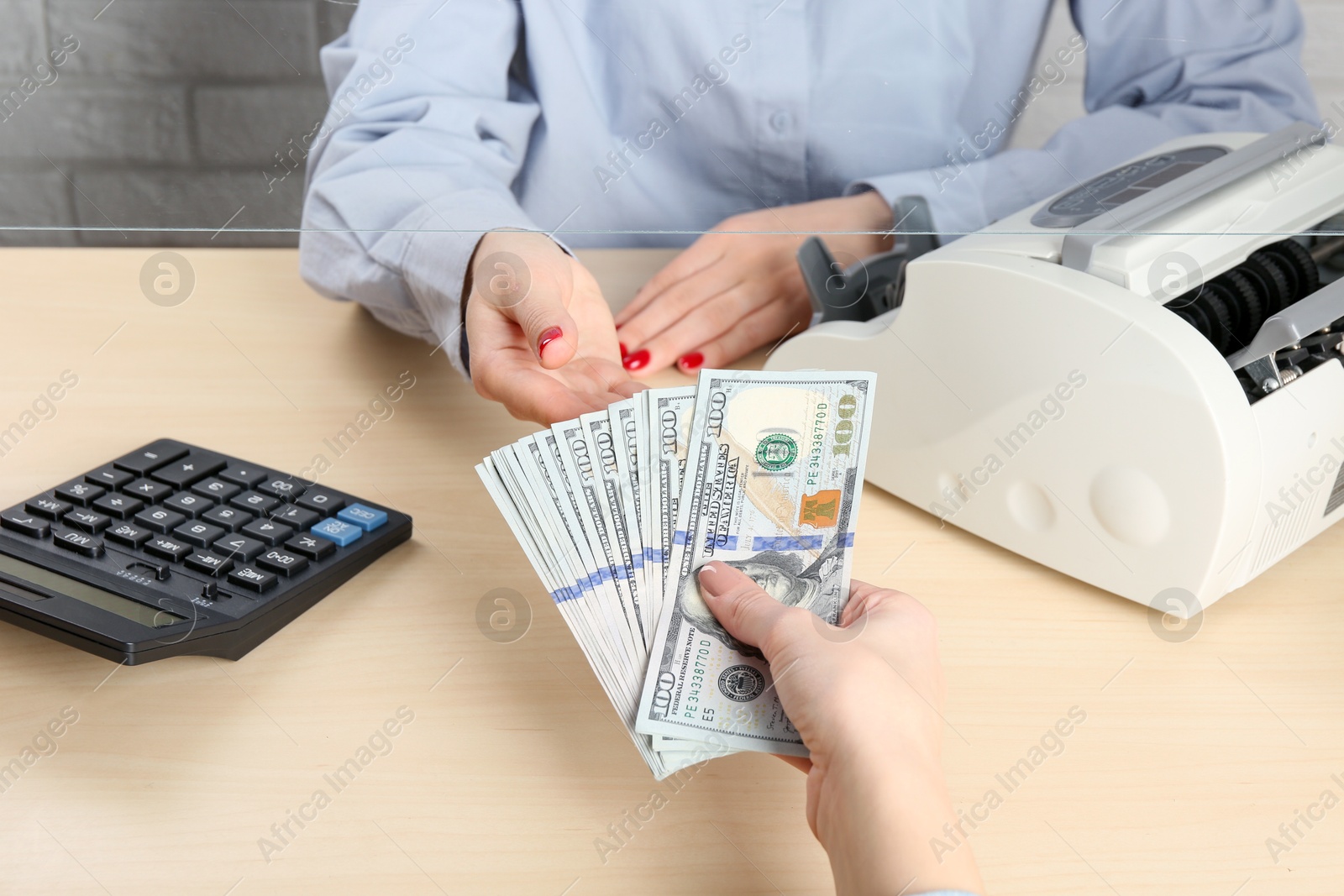 Photo of Client giving dollar banknotes to cashier at table in money exchange, closeup