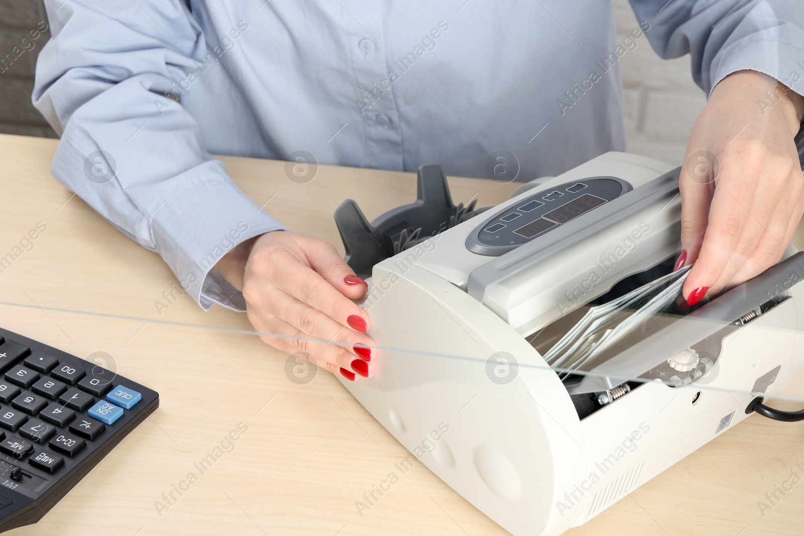 Photo of Cashier using money counting machine at table in currency exchange, closeup