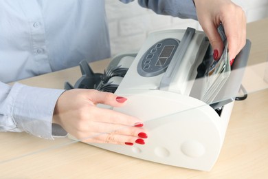 Photo of Cashier using money counting machine at table in currency exchange, closeup