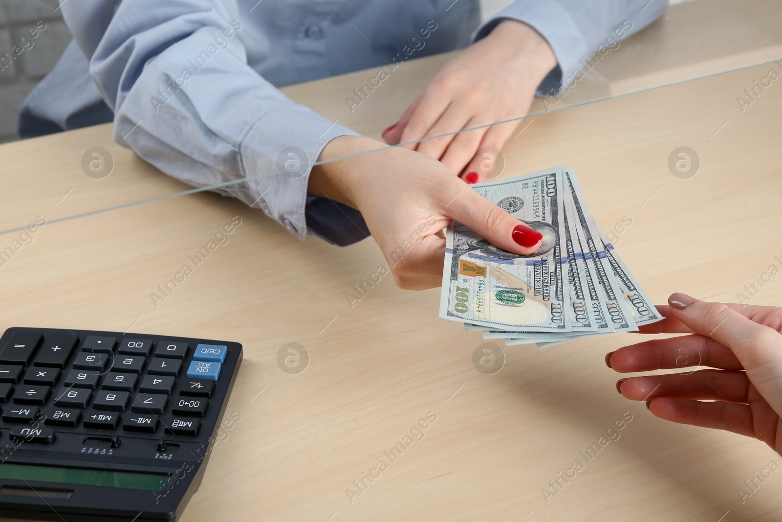 Photo of Cashier giving dollar banknotes to client at table in money exchange, closeup