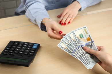 Photo of Client giving dollar banknotes to cashier at table in money exchange, closeup