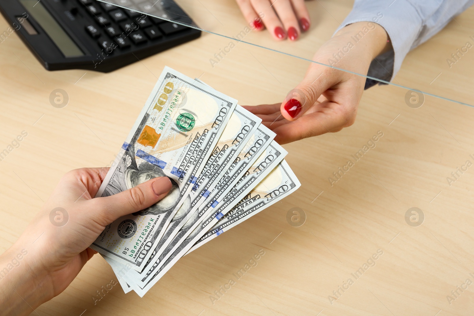 Photo of Client giving dollar banknotes to cashier at table in money exchange, closeup