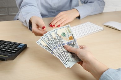 Photo of Client giving dollar banknotes to cashier at table in money exchange, closeup