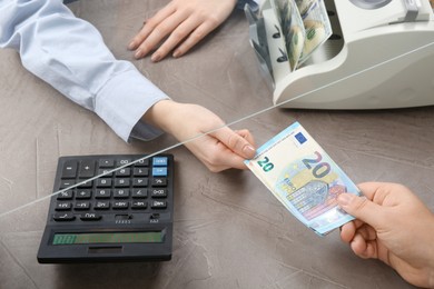 Photo of Client giving euro banknotes to cashier at table in money exchange, closeup