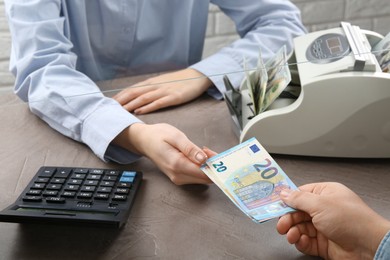 Photo of Client giving euro banknotes to cashier at table in money exchange, closeup