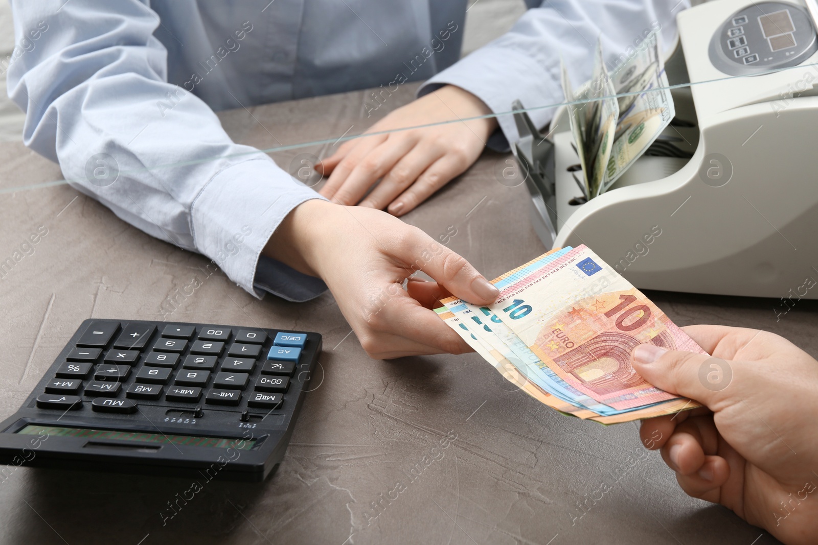 Photo of Client giving euro banknotes to cashier at table in money exchange, closeup