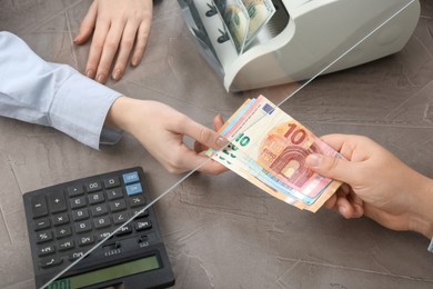 Photo of Client giving euro banknotes to cashier at table in money exchange, closeup