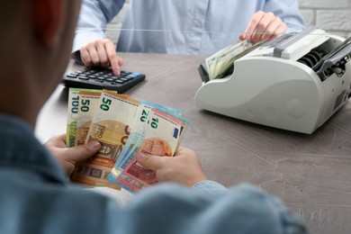 Photo of Client counting money at table in currency exchange, closeup