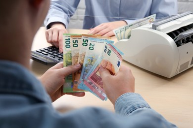 Photo of Client counting money at table in currency exchange, closeup