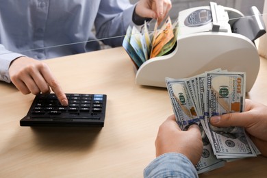 Photo of Client counting money at table in currency exchange, closeup