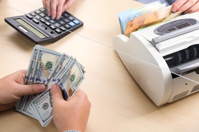 Photo of Client counting money at table in currency exchange, closeup