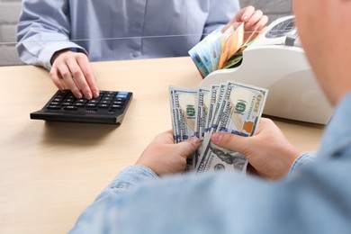 Photo of Client counting money at table in currency exchange, closeup