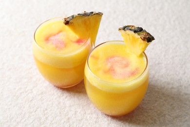 Photo of Tasty pineapple cocktail in glasses served on white table, closeup