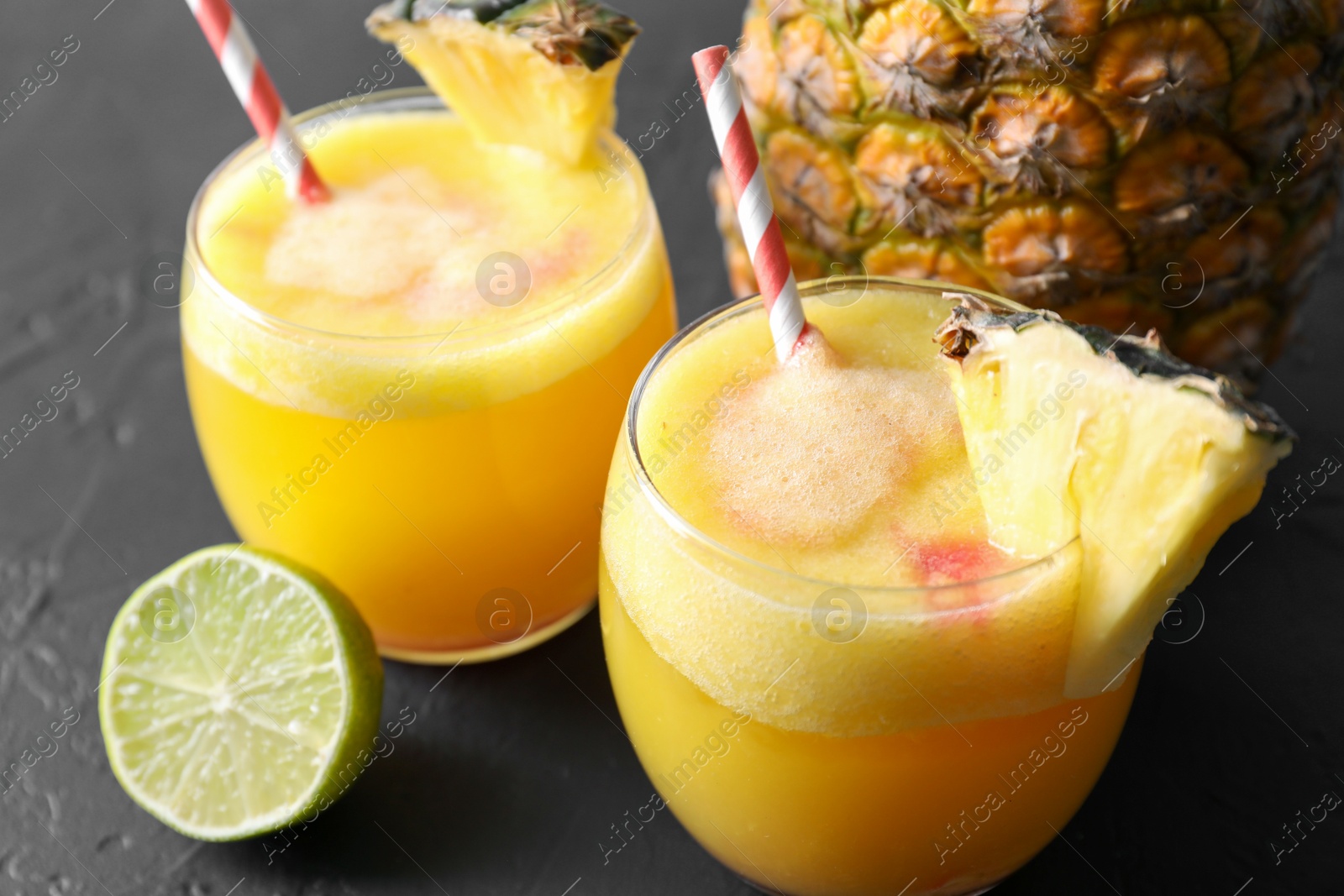 Photo of Tasty pineapple cocktail in glasses served on black table, closeup