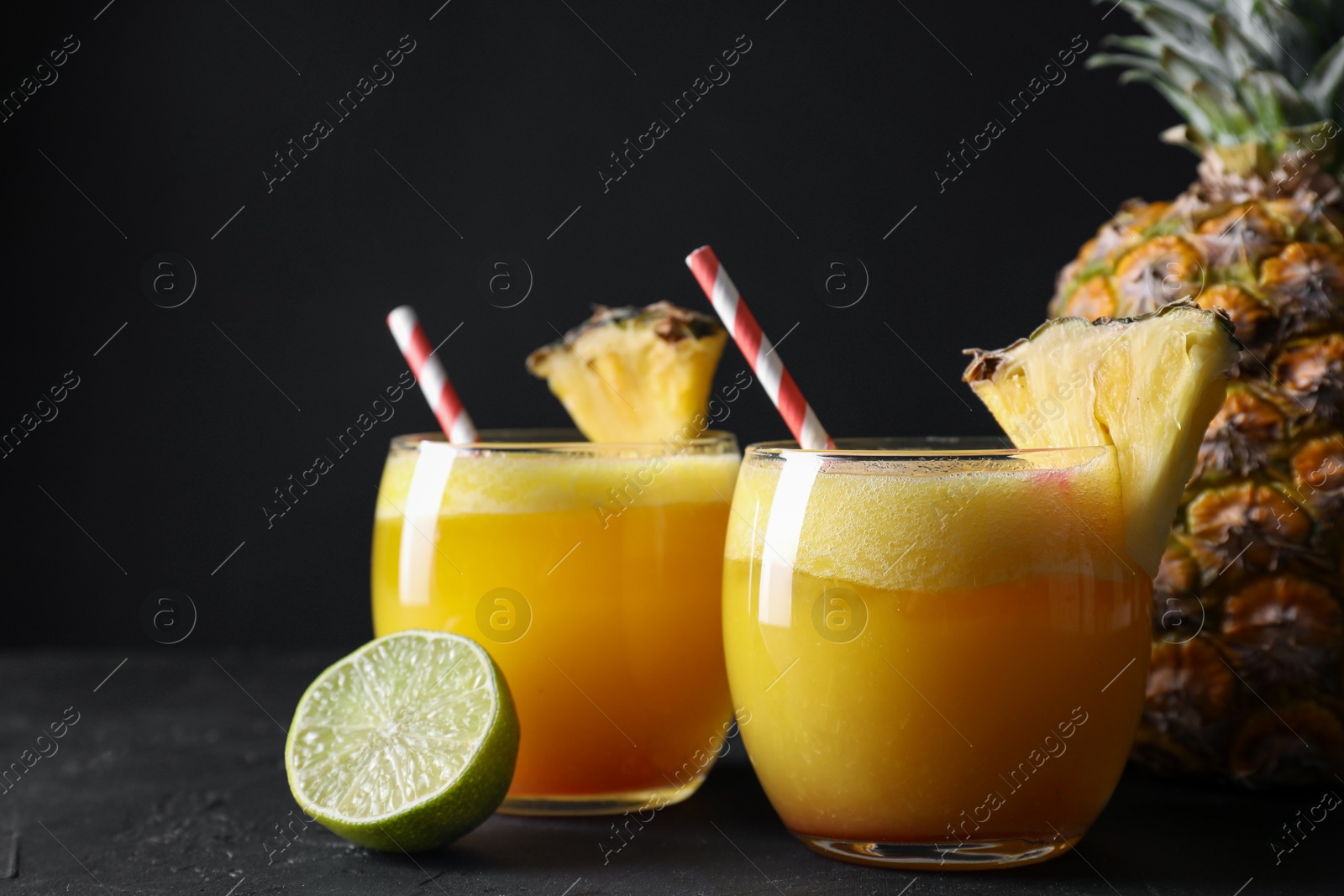 Photo of Tasty pineapple cocktail in glasses served on black table, closeup