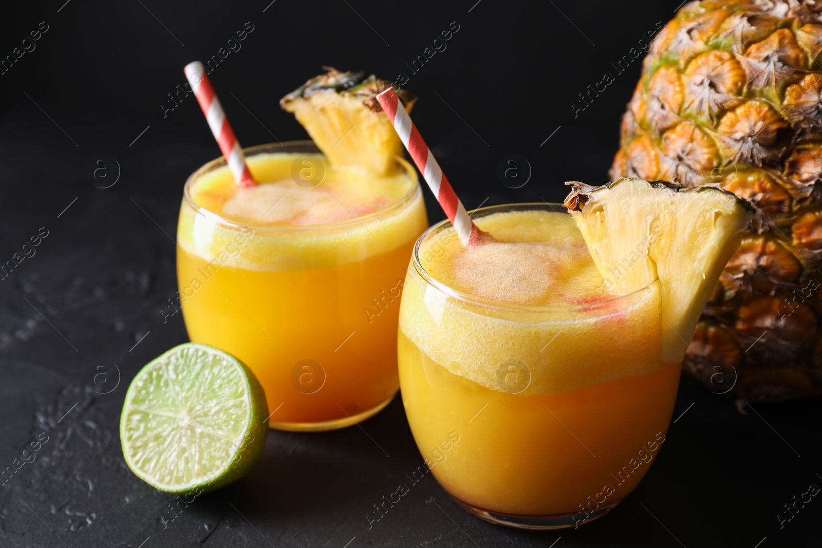 Photo of Tasty pineapple cocktail in glasses served on black table, closeup