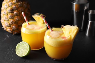 Photo of Tasty pineapple cocktail in glasses served on black table