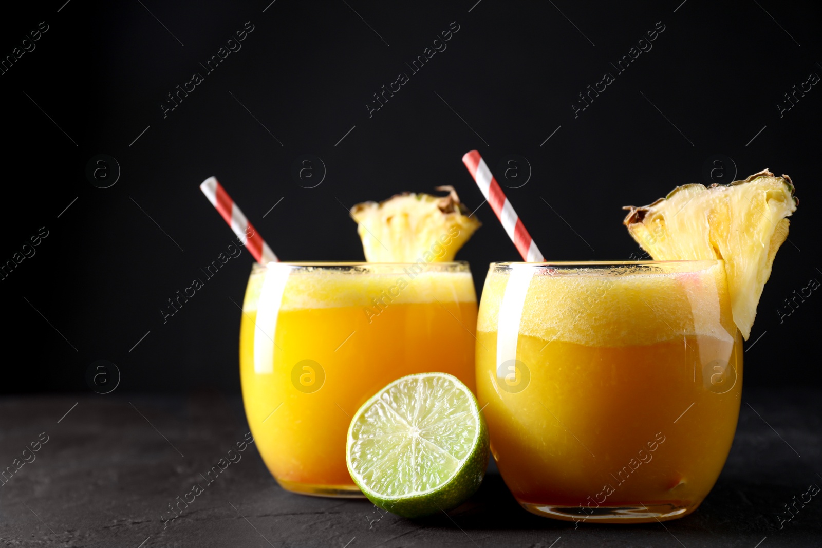 Photo of Tasty pineapple cocktail in glasses served on black table, closeup