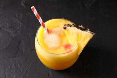 Photo of Tasty pineapple cocktail in glass served on black table, closeup