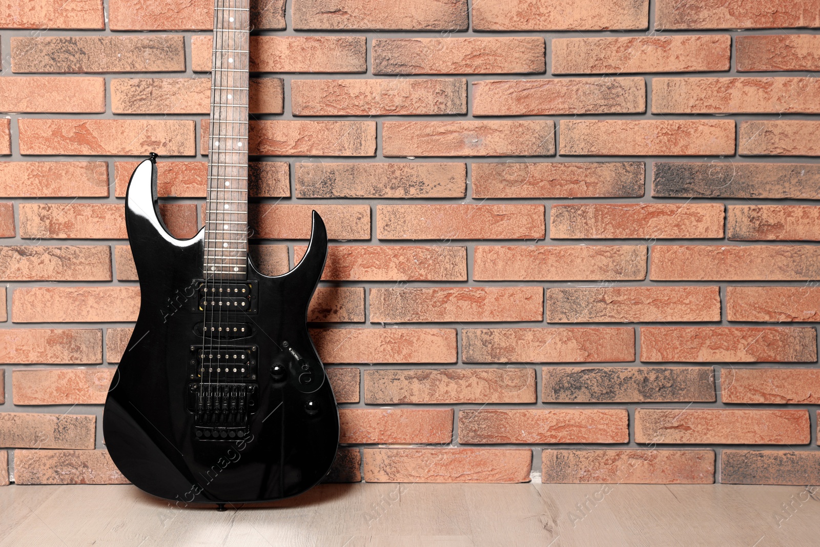 Photo of One modern electric guitar near brick wall. Space for text