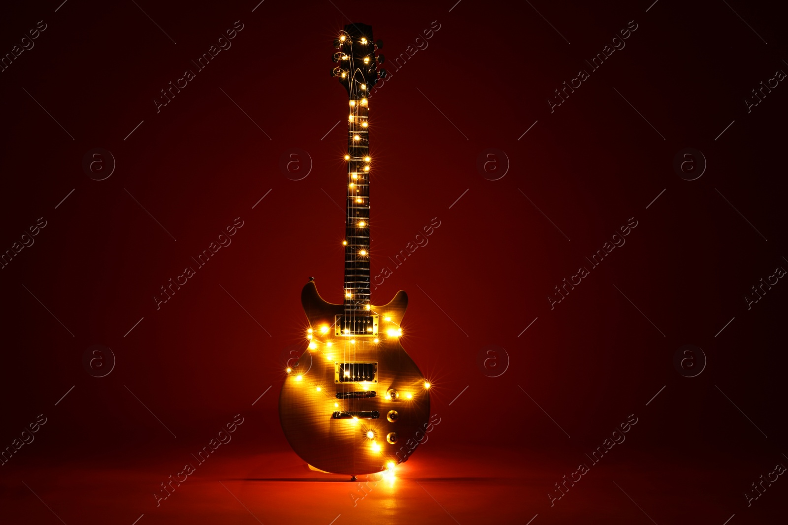 Photo of Electric guitar with Christmas lights on dark red background