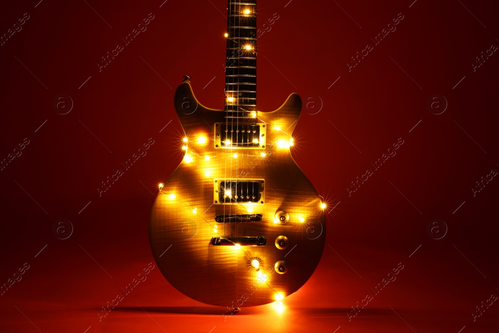 Photo of Electric guitar with Christmas lights on dark red background