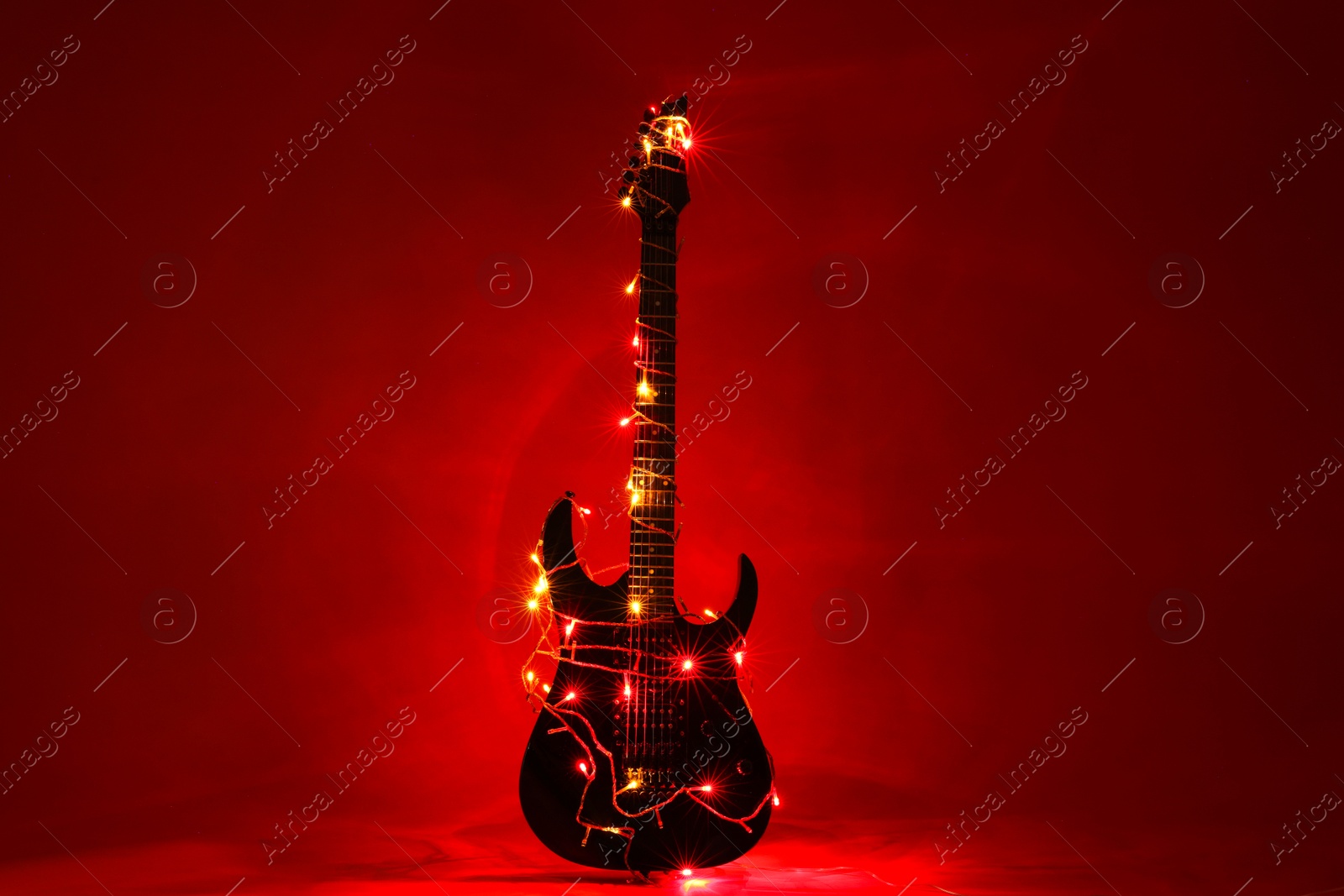 Photo of Electric guitar with Christmas lights on dark red background