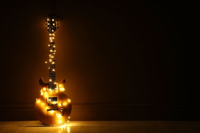 Photo of Electric guitar with Christmas lights on dark background. Space for text