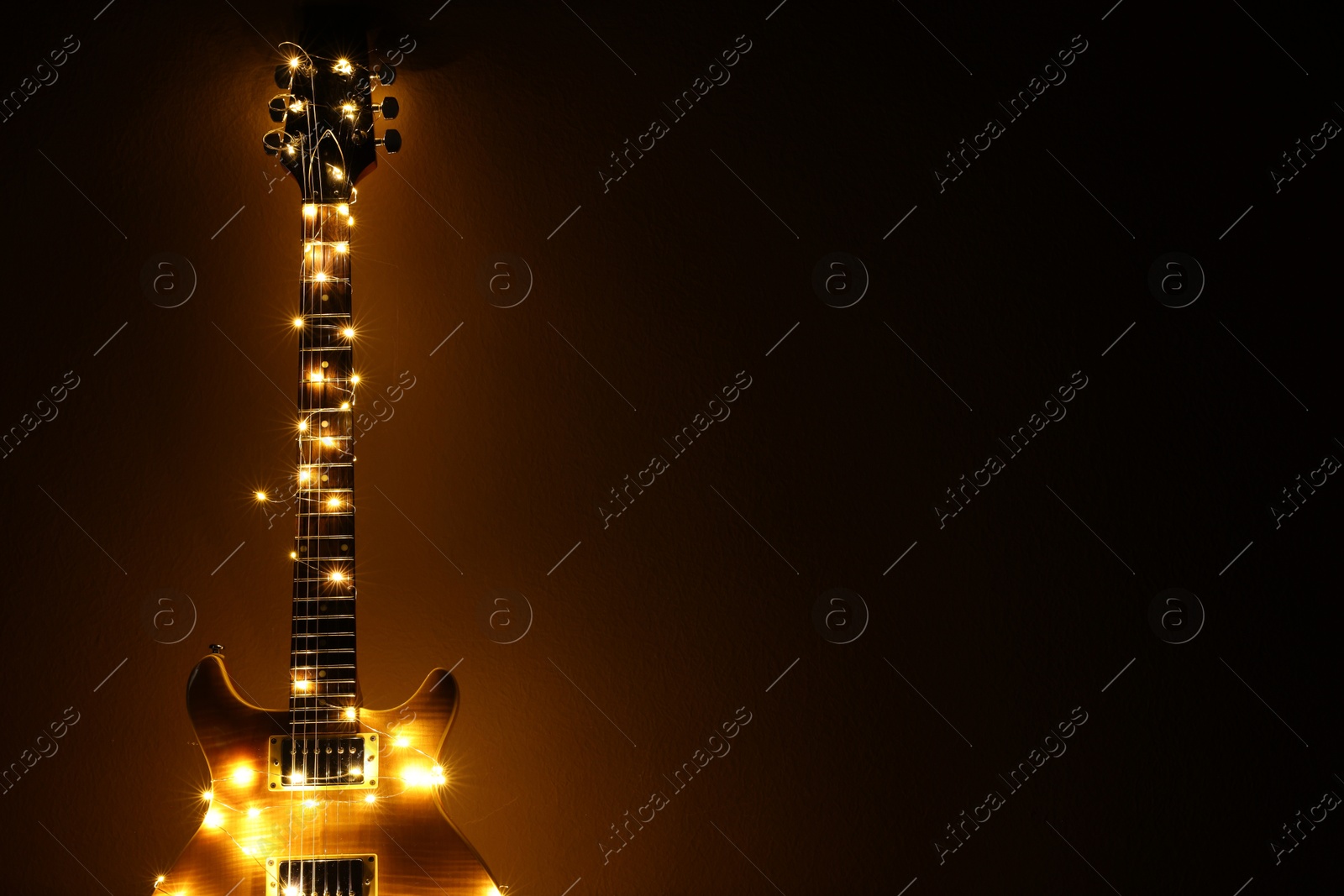 Photo of Electric guitar with Christmas lights on dark background. Space for text