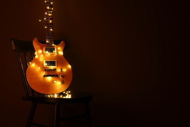 Electric guitar with Christmas lights on chair against dark background. Space for text