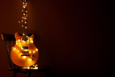 Electric guitar with Christmas lights on chair against dark background. Space for text