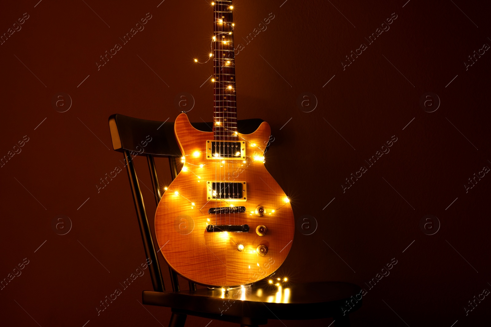 Photo of Electric guitar with Christmas lights on chair against dark background