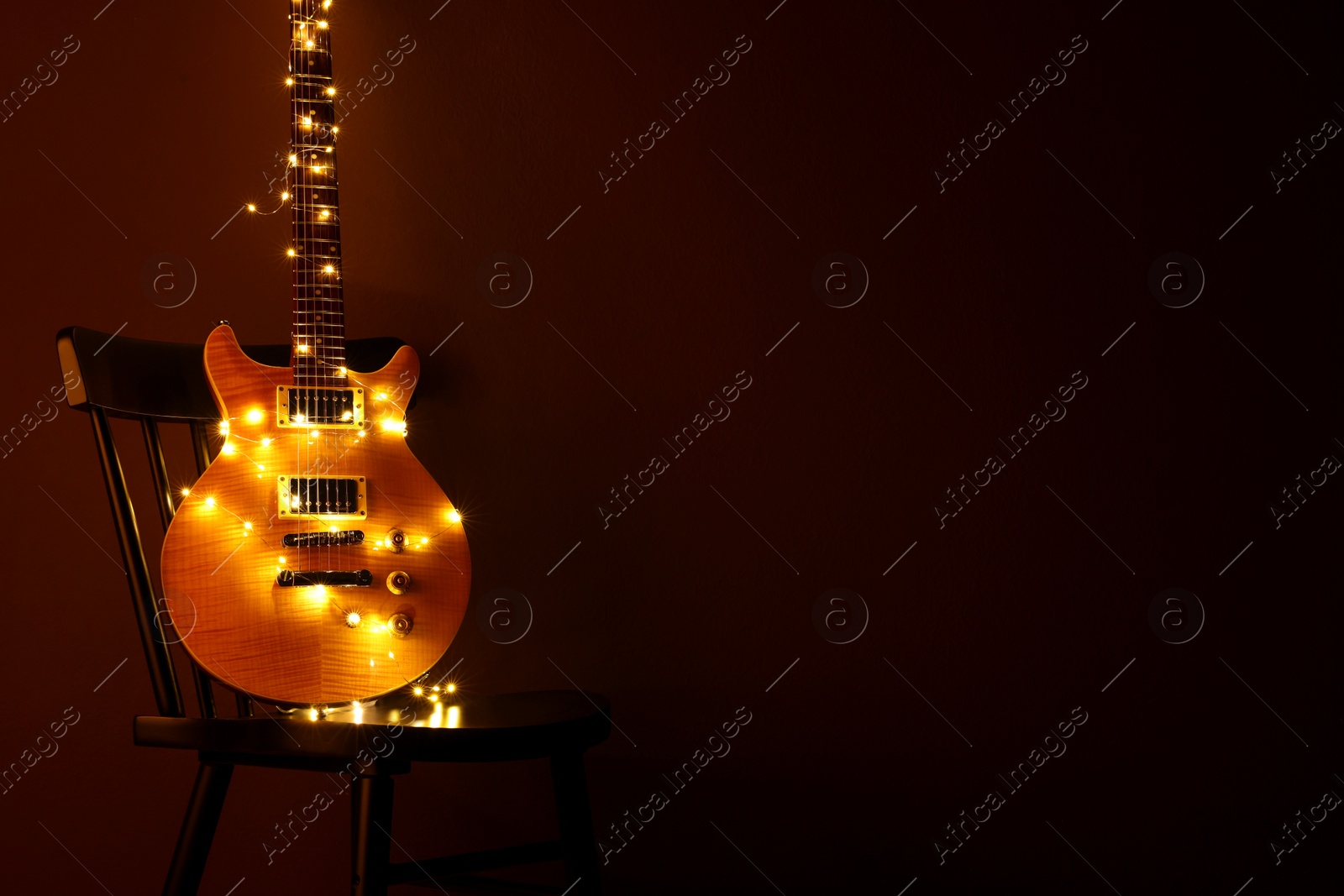 Photo of Electric guitar with Christmas lights on chair against dark background. Space for text