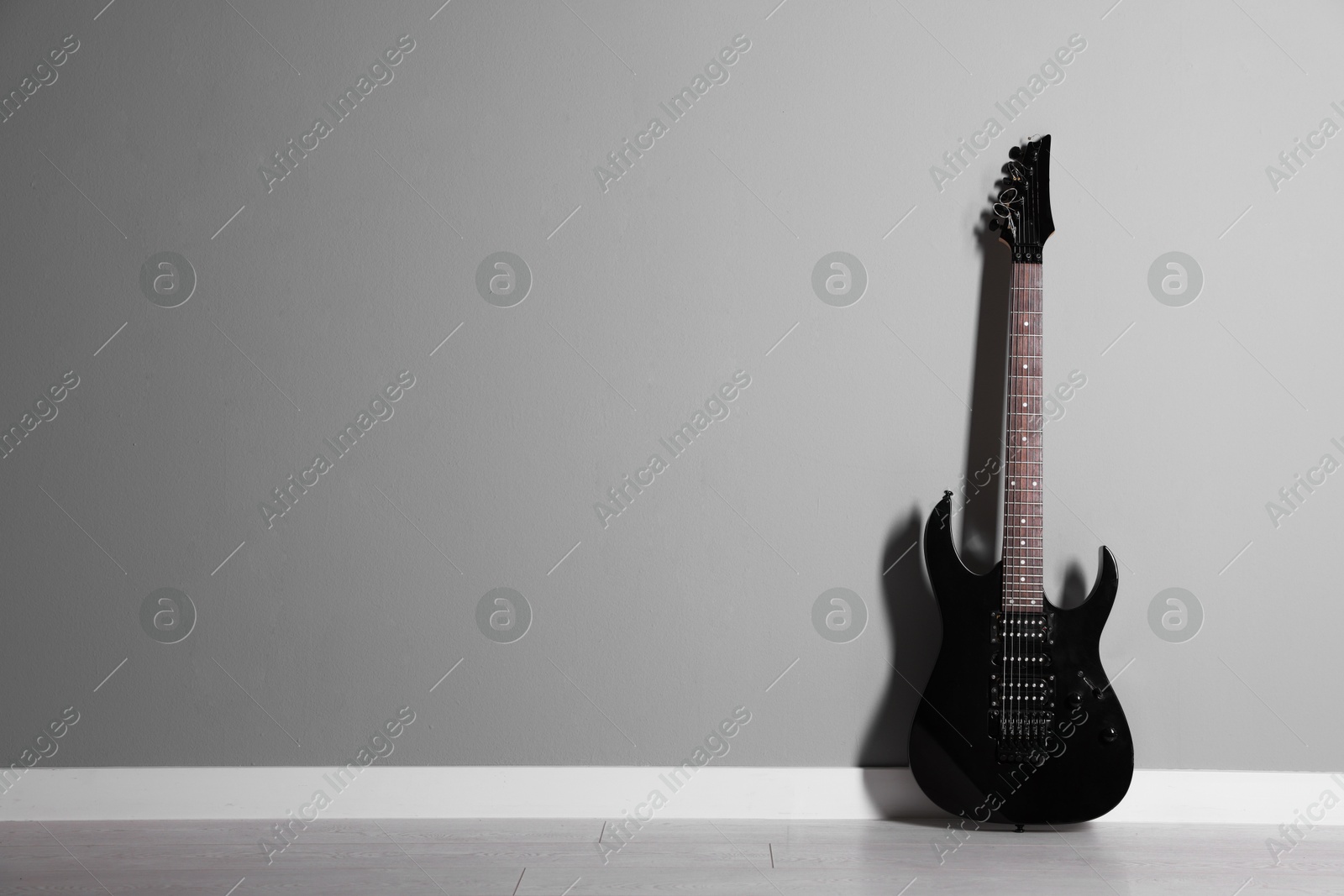 Photo of One modern electric guitar near light grey wall. Space for text