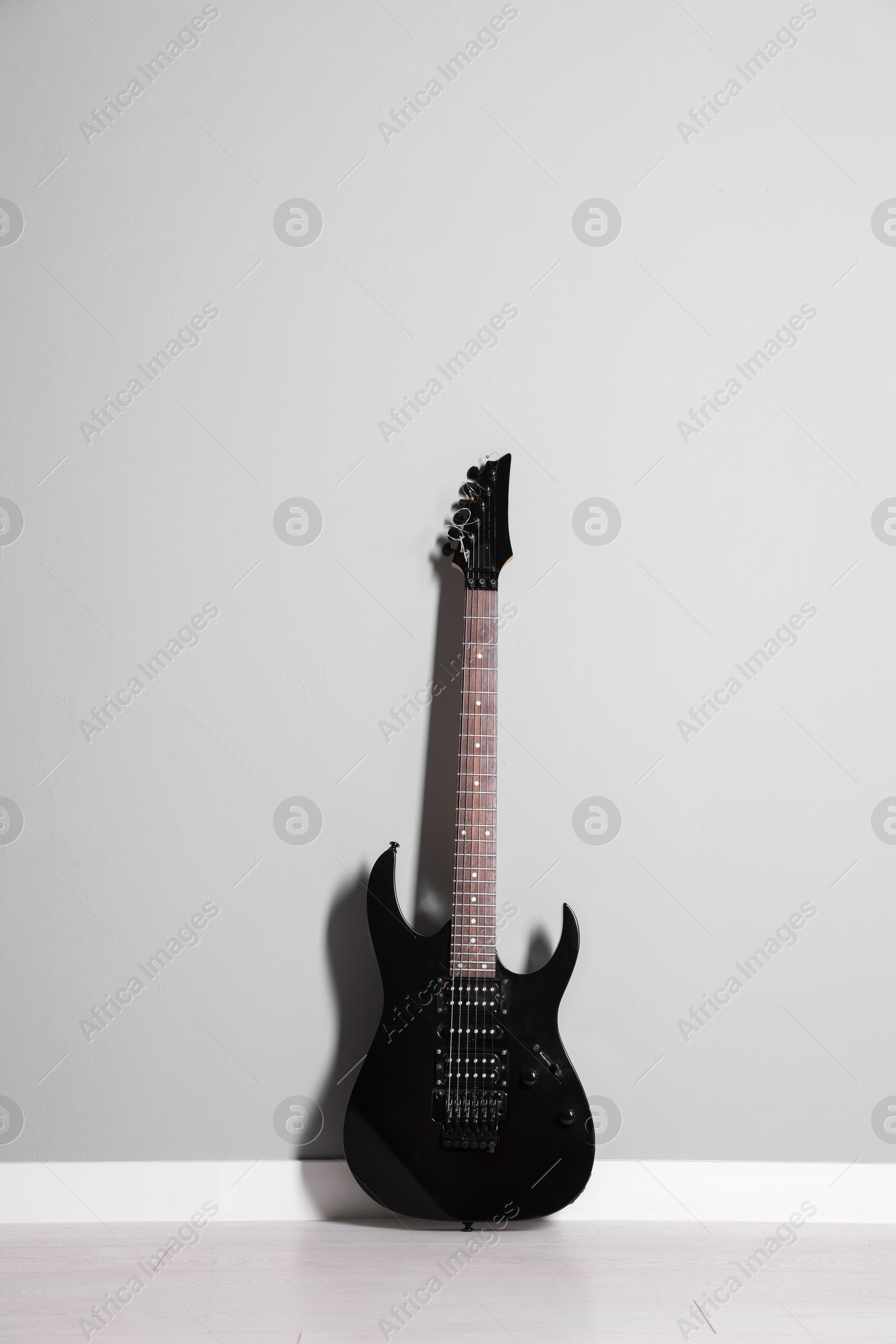 Photo of One modern electric guitar near light grey wall