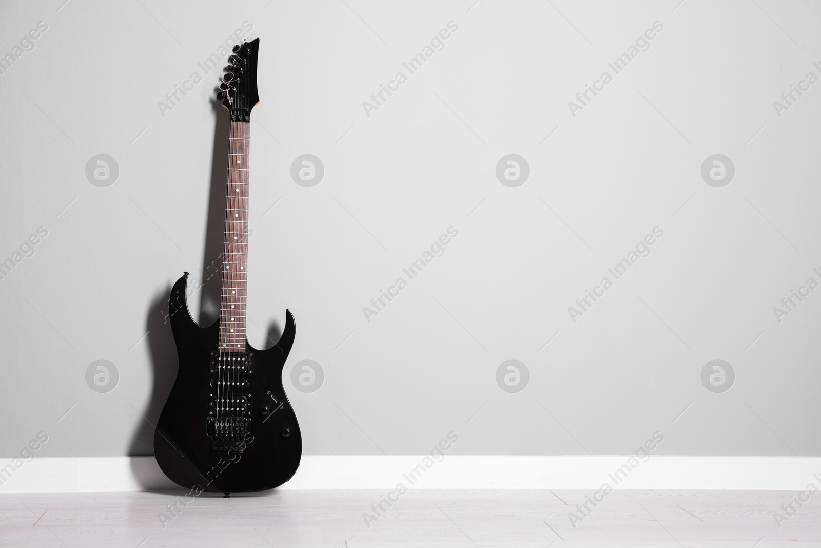 Photo of One modern electric guitar near light grey wall. Space for text