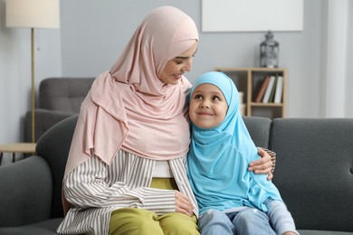 Muslim mother and her daughter sitting on sofa at home