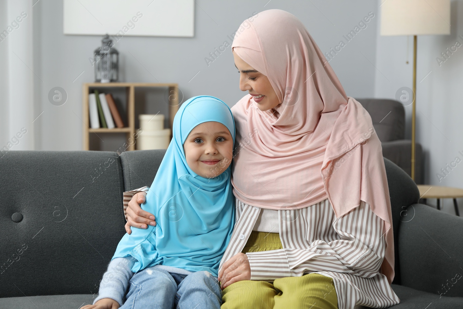 Photo of Muslim mother and her daughter sitting on sofa at home