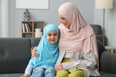 Photo of Muslim mother and her daughter sitting on sofa at home