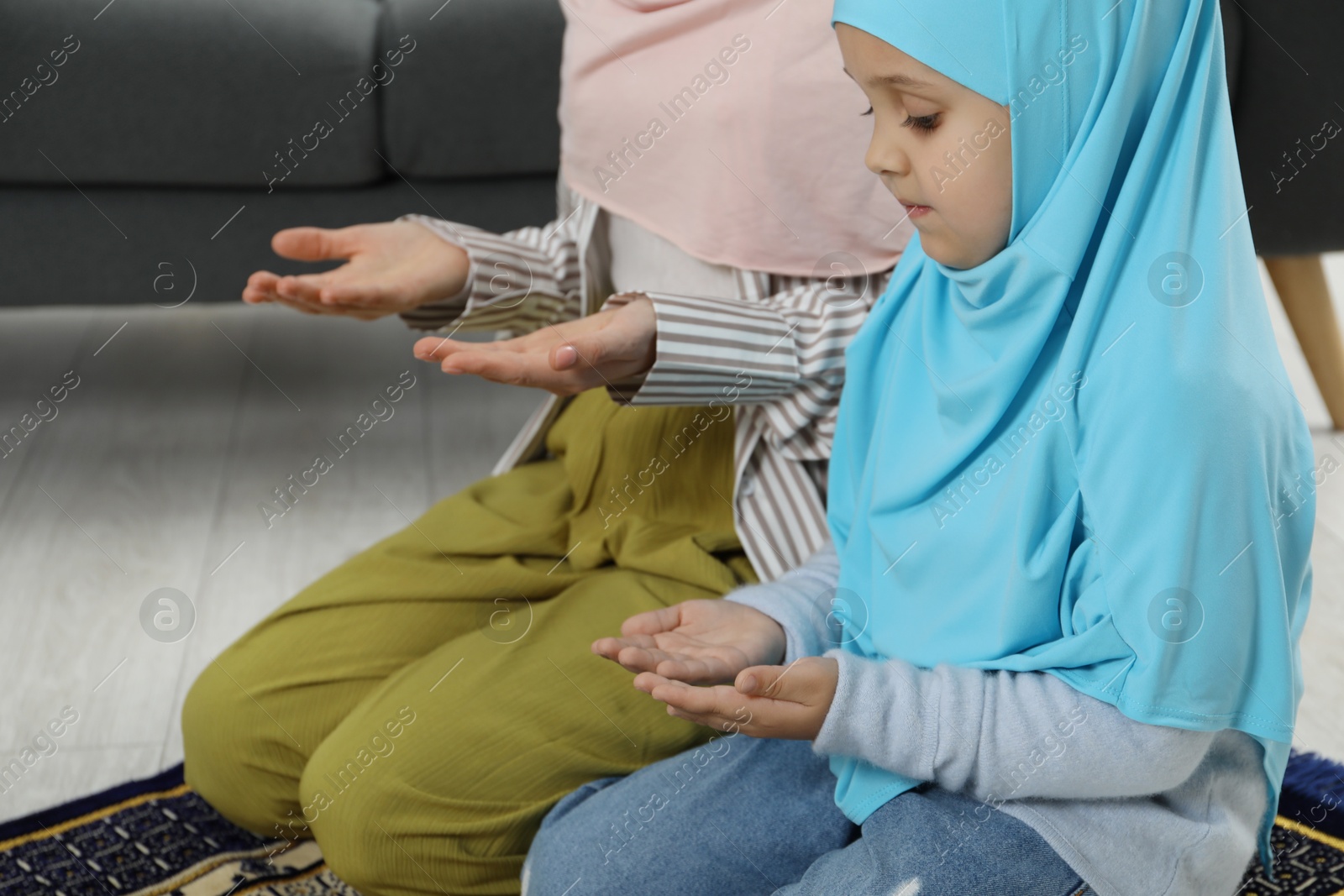 Photo of Muslim woman and her daughter praying on mat at home, closeup