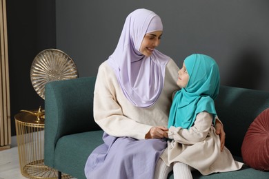 Photo of Muslim woman and her daughter sitting on sofa at home