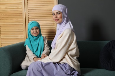 Muslim woman and her daughter sitting on sofa at home