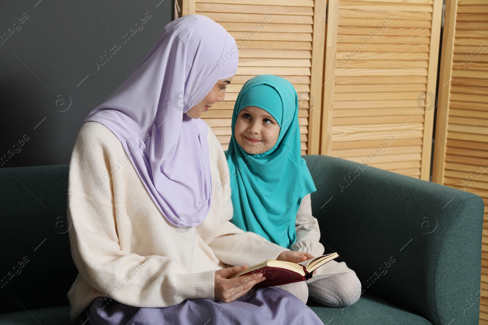 Photo of Muslim woman and her daughter reading Quran at home