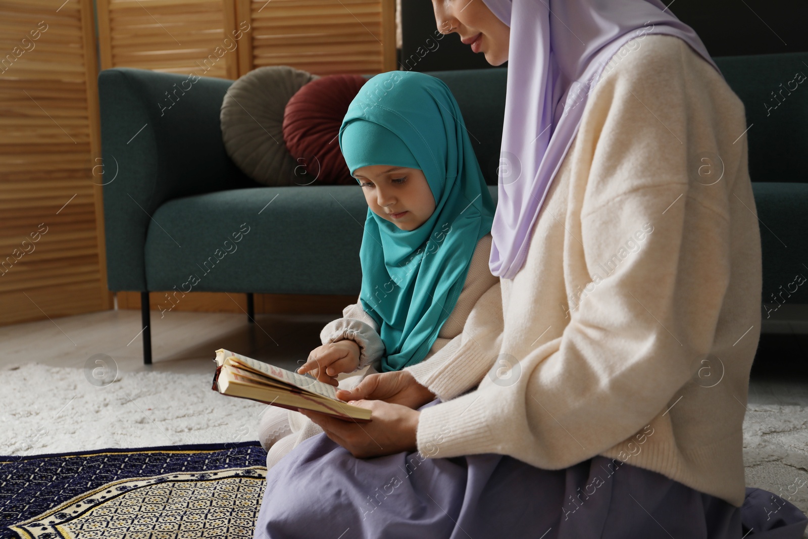 Photo of Muslim woman and her daughter with Quran praying on mat at home